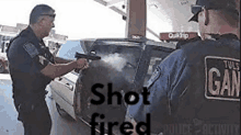 a police officer is holding a gun in front of a car with the words shot fired on the bottom .