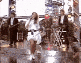 a woman in a white dress is singing into a microphone in front of a band on a stage .