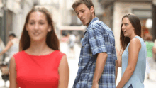 a man in a plaid shirt is walking down a street while a woman in a red dress looks on