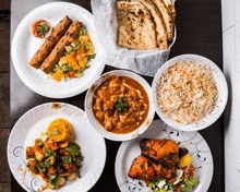 a table topped with plates of food including rice , chicken , vegetables and naan bread .