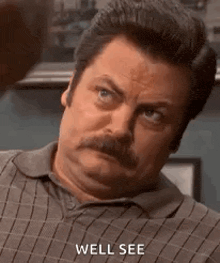 a man with a mustache is sitting down and making a funny face while saying `` well see '' .