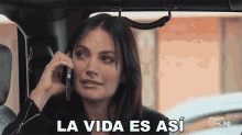 a woman sitting in a car talking on a cell phone with the words la vida es asi written on the bottom