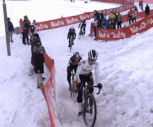 a group of people riding bicycles in the snow with a red fence that says ' valentin ' on it