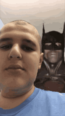 a bald man in a blue shirt is taking a selfie with a picture of batman behind him