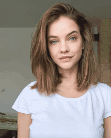 a woman wearing a white t-shirt looks at the camera with a brick wall in the background