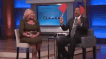 a man in a suit and tie is holding a red heart while sitting next to a woman in a chair