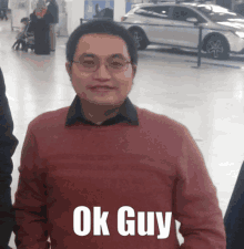 a man in a red sweater stands in front of a car that says ok guy