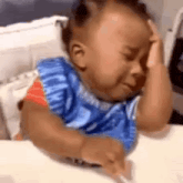 a baby is crying while sitting at a table with his hands on his head .