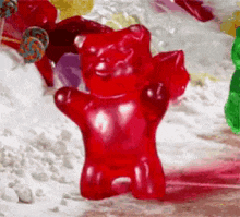 a red gummy bear is sitting on a pile of candy