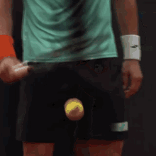 a man in a green shirt and black shorts is holding a tennis racket and a tennis ball .