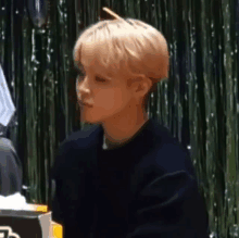 a young man with blonde hair is sitting at a table with a box of tissues .