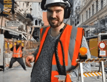 a man wearing an orange vest and a hard hat stands in front of a sign that says under construction