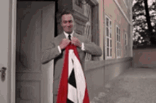 a man in a suit and tie is holding a red white and black flag in front of a building .