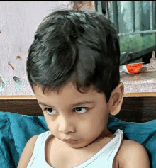 a young boy in a white tank top is sitting on a bed .