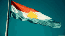 a red white and blue kurdish flag is flying in the wind against a blue sky