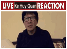 a man wearing glasses is sitting on a couch in front of a sign that says `` live ke huy quan reaction '' .