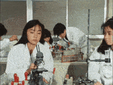 a woman is looking through a microscope in a lab while a group of people work in the background .