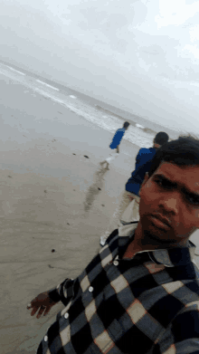 a man in a plaid shirt takes a picture of himself on the beach