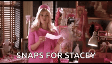 a woman in a pink dress is holding a piece of paper and the words snaps for stacey are written on the screen .
