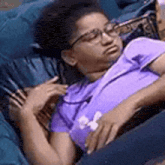a woman in a purple shirt is laying on a blue couch .