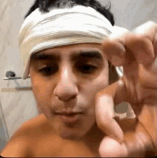 a man with a bandage on his head is pointing at the camera with his finger .