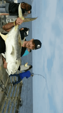 a man holding a large fish on a pier with people fishing in the background and a sign that says ' bridge ' on it