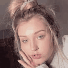 a close up of a woman 's face with her hand on her face and a bun in her hair .