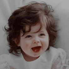 a little girl with brown hair is smiling with her mouth open .