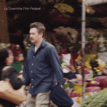 a man in a blue shirt is walking in front of a display of flowers with the words la guarimba film festival below him