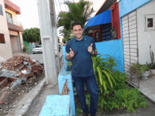 a man giving a thumbs up in front of a blue building