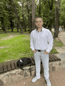 a man in a white shirt stands in front of a park