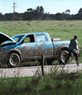 a man is pushing a muddy truck that has a sticker on the back that says ' emergency assistance '