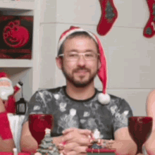 a man wearing a santa hat and glasses is sitting at a table with a christmas tree in front of him .