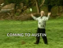 a man holding a badminton racket in a grassy field with the words " coming to austin " behind him