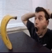 a man is sitting at a table with his mouth open and a banana on the table .