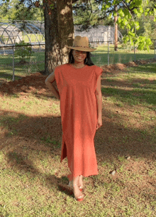 a woman wearing an orange dress and a straw hat stands in a field