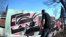 a man in a black shirt is standing in front of a wall with graffiti on it that says ecru