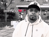 a man wearing a hat and a hoodie is standing in front of a brick building with the words ihynld above him