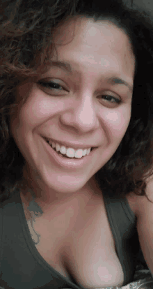 a woman with curly hair and a tattoo on her chest smiles for the camera