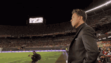 a man in a suit stands on a soccer field in front of a sign that says ' budget '