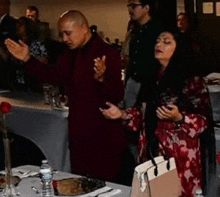 a group of people are standing around a table with their arms outstretched in prayer .