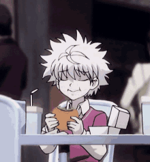 a boy with white hair is sitting at a table eating a hamburger and drinking juice .