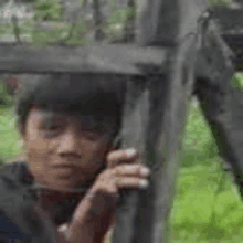 a young boy is standing behind a wooden fence talking on a cell phone .