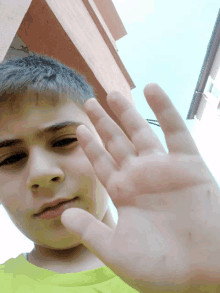 a young boy in a yellow shirt holds his hand up in front of his face