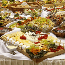 a buffet table filled with lots of food including cheese , grapes , tomatoes , and bread .