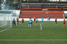 a group of soccer players are playing on a field with a sign that says sport in the background