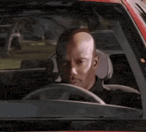 a man with a bald head is driving a car and looking at the camera