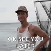 a man wearing a hat and a tank top is standing on a boat in the water .