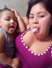 a woman in a purple tank top holds a baby who is sticking his tongue out