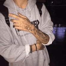 a person with a tattoo on their hand and arm is wearing a hoodie and headphones .